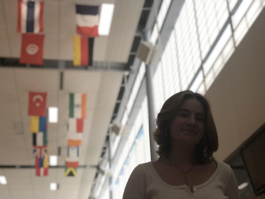 Gaby, a transfer student from France, walks the art hallway with international flags swaying above her.