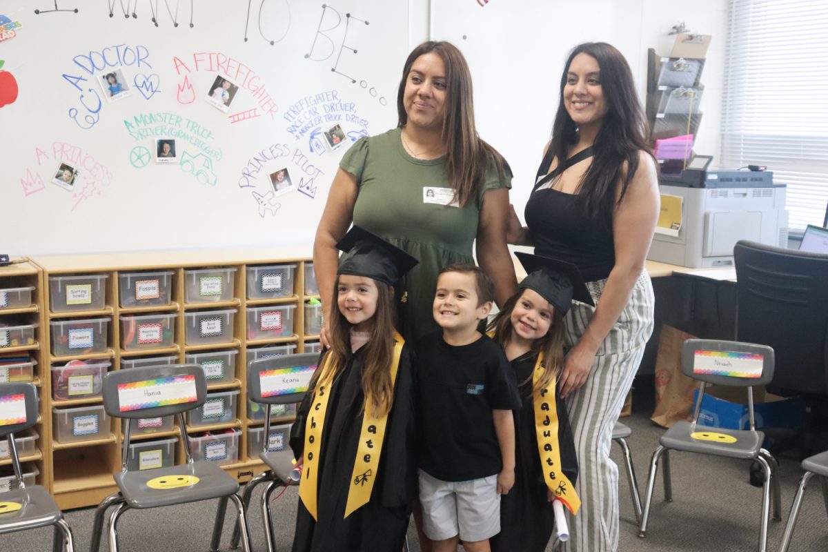 Three preschoolers pose proudly with their parents, showing off their graduation robes after the parade. 
