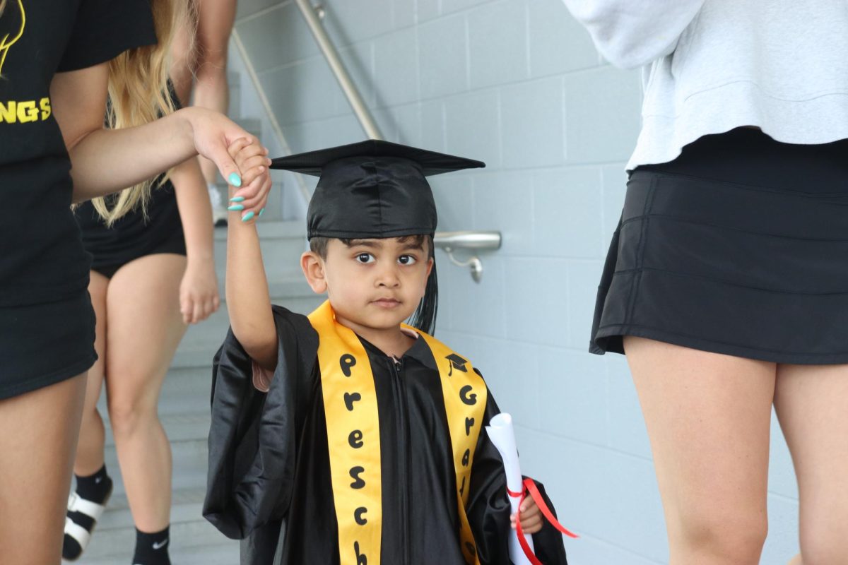 A preschooler walks along with their student partners, waving off to the crowd.