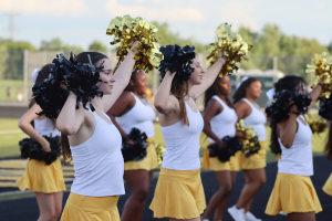 The dance team performs together to the audience as the American football scrimmage happens behind them, awaiting for the half-time stop.